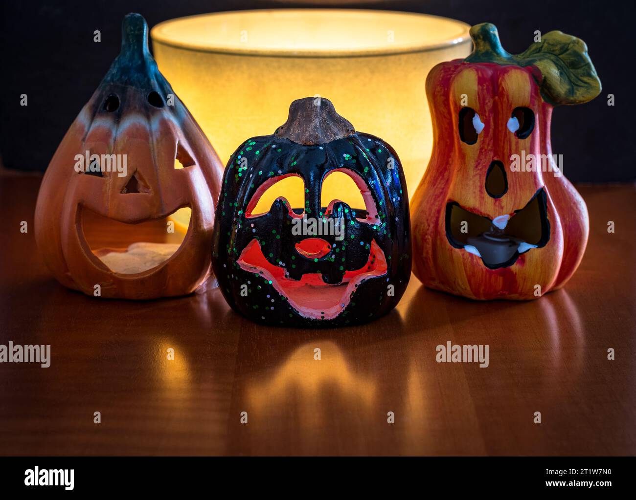 Three small and funny Halloween pumpkins with a large warm light candle behind. Decorations placed on a wooden surface with a black background. Stock Photo