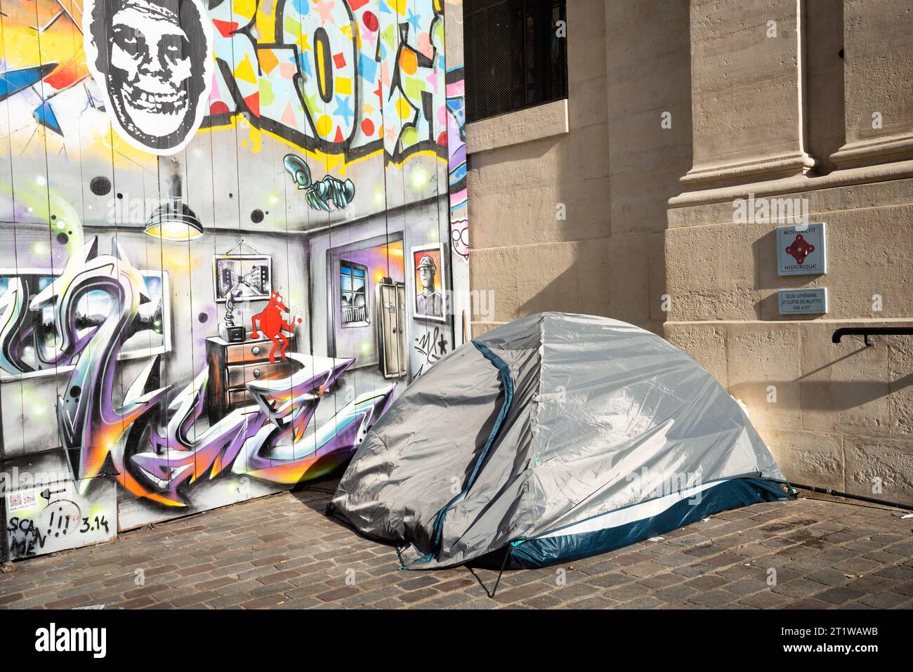 Paris, France - February 21, 2023: Social contrsts. Tent of homeless person, apartment graffiti and plate of Historic Monument (belonging to a church) Stock Photo