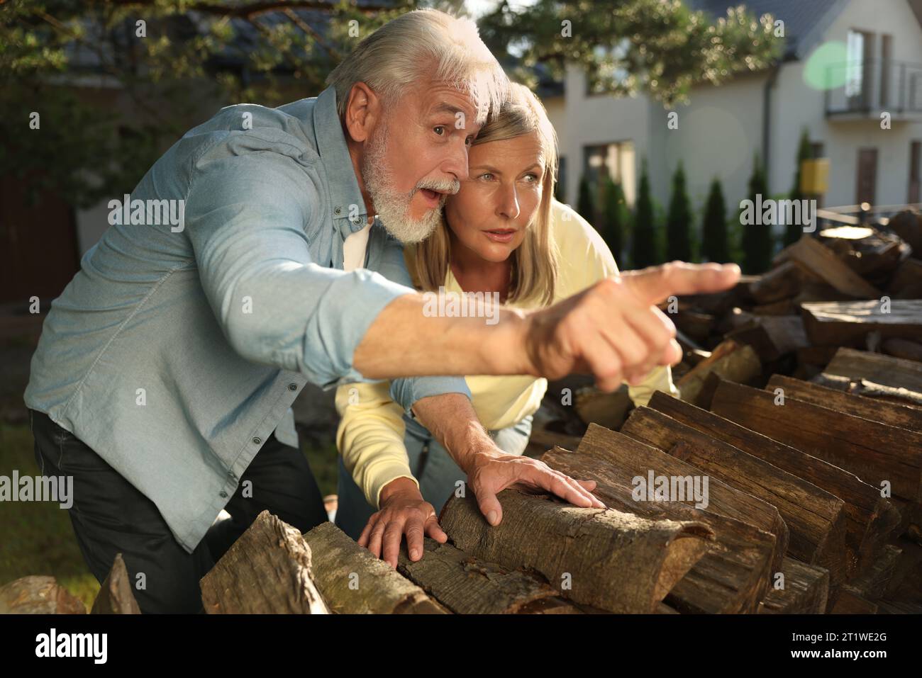 Concept of private life. Curious senior couple spying on neighbours over firewood outdoors Stock Photo