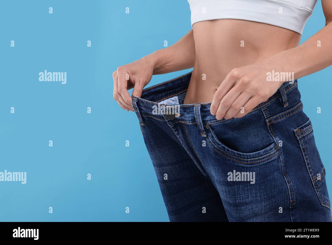 Slim woman wearing big jeans on light blue background, closeup and space for text. Weight loss Stock Photo