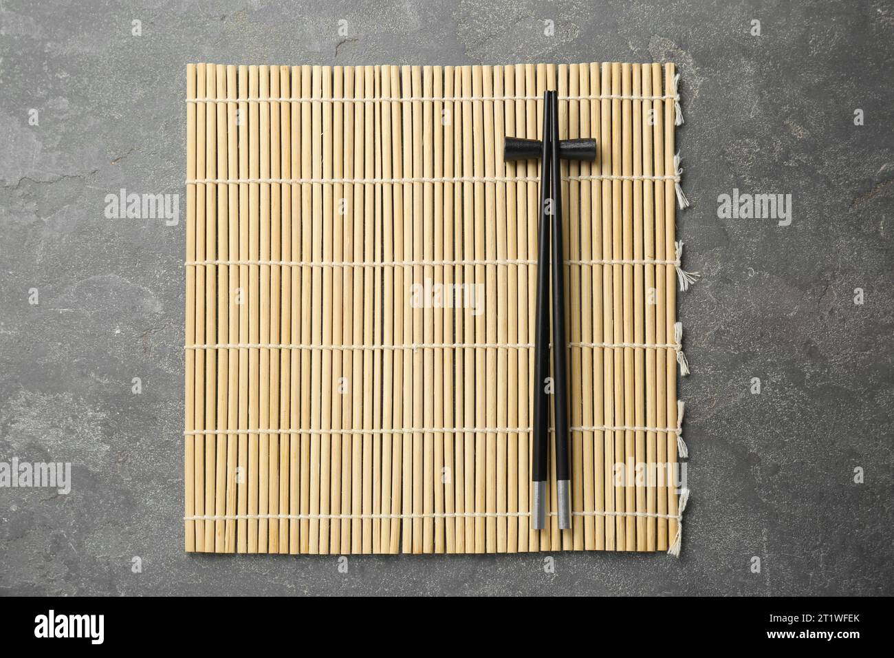 https://c8.alamy.com/comp/2T1WFEK/bamboo-mat-with-pair-of-black-chopsticks-and-rest-on-grey-table-top-view-2T1WFEK.jpg