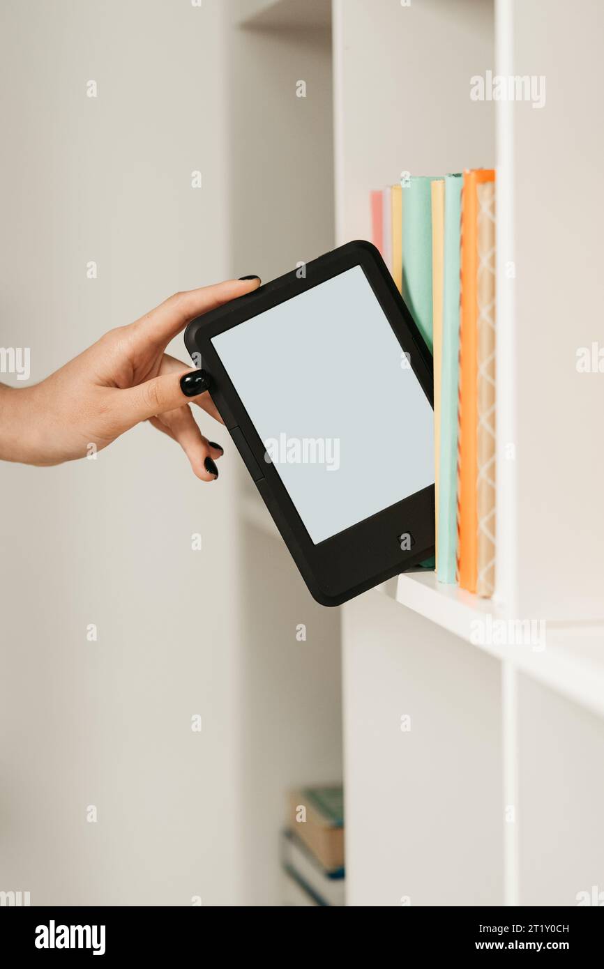 Man taking modern e-book reader from a bookshelf close up Stock Photo