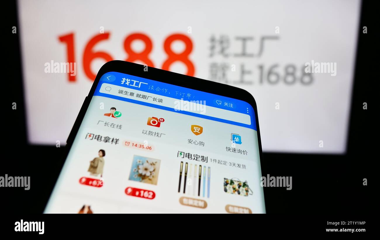 Mobile phone with website of Chinese online shop 1688.com (Alibaba) in front of business logo. Focus on top-left of phone display. Stock Photo