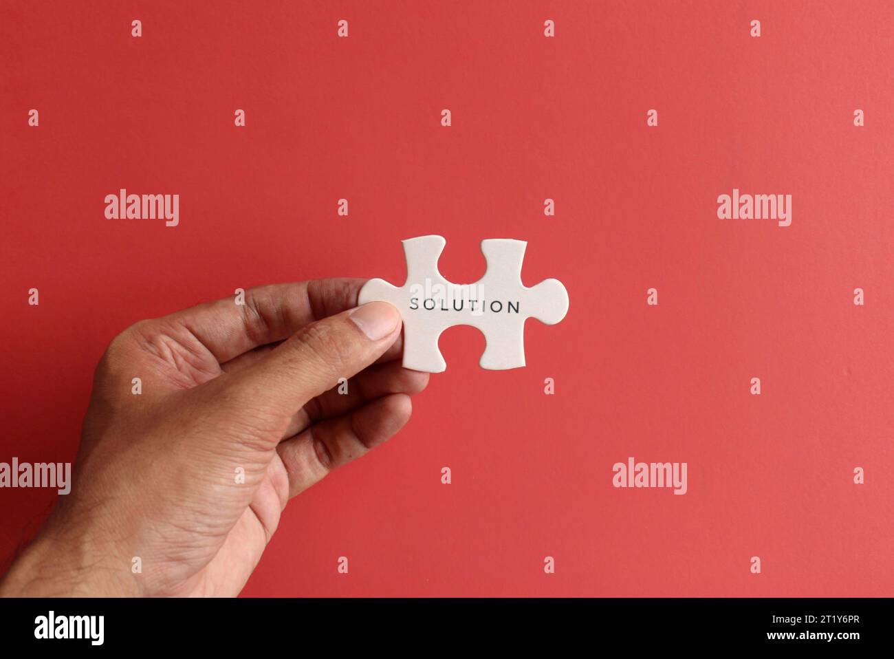 Hand holding puzzle pieces with text SOLUTION on red background. Stock Photo