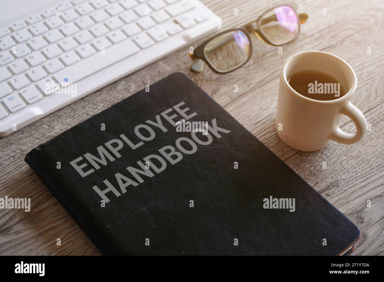 Closeup image of book with text EMPLOYEE HANDBOOK surrounded by cup of coffee and glasses on office desk Stock Photo