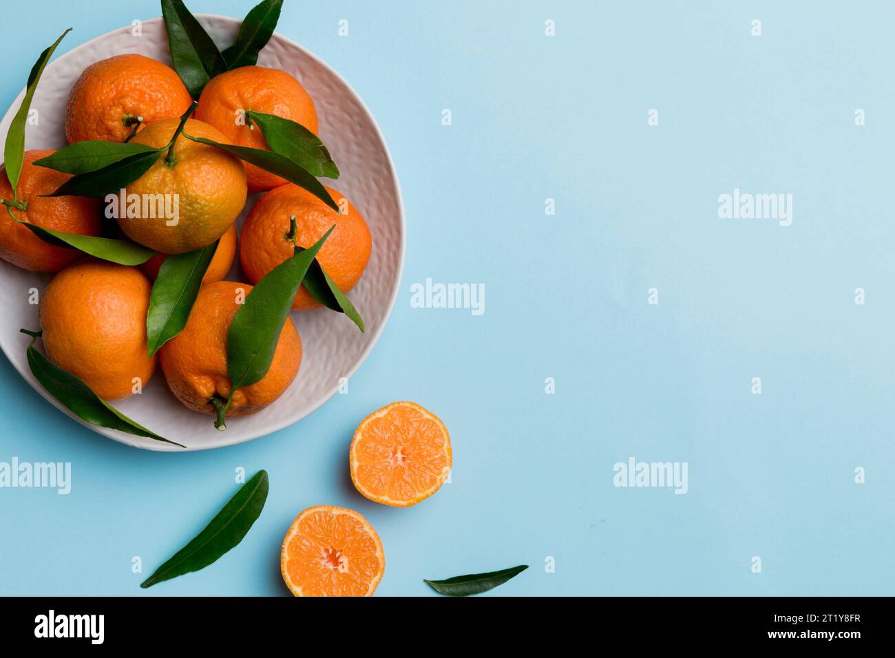Fresh cutted clementines and whole mandarin over round plate on colored