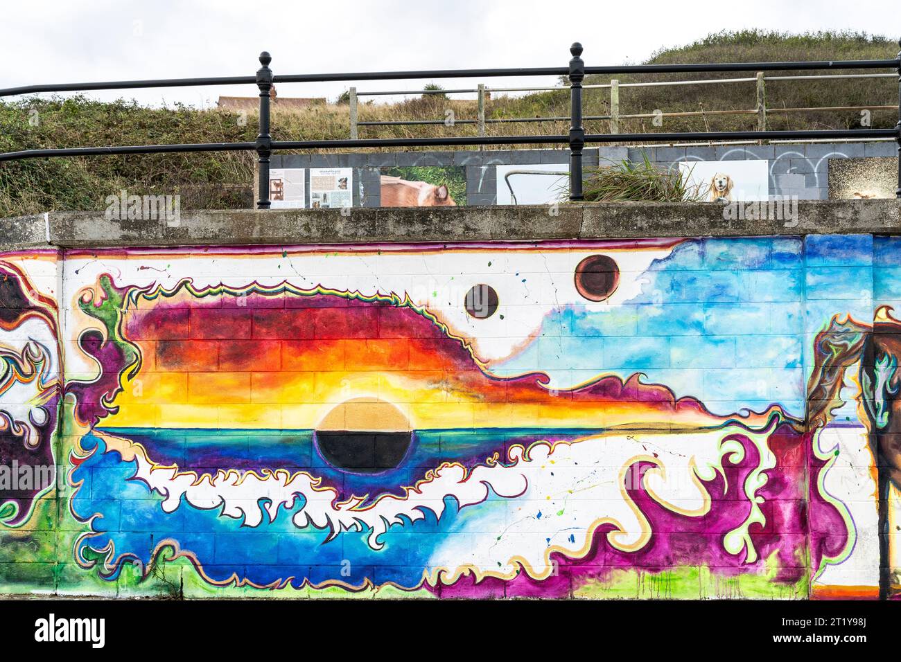 Seafront graffiti on a seawall at Herne Bay. Horizon with the sunset and yellow and red sky above and below the sea and the dark sun below the horizon. Painted by an unknown young woman, the painting is one of a series interlinked by a common horizon along the wall. Stock Photo