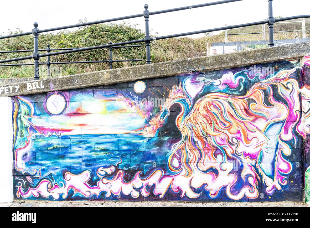 Seafront graffiti on a seawall at Herne Bay in the form of a highly detailed painting of a fire breathing dragon at the edge of the sea with a white moons or suns above. Painted by an unknown young woman. The painting is one of a series interlinked by a common horizon along the wall. Stock Photo