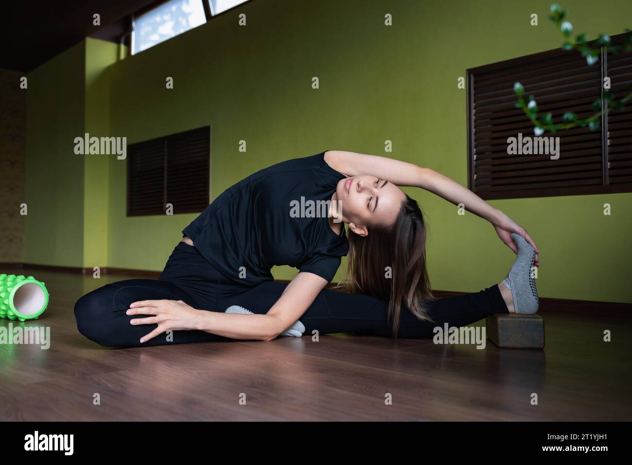 A young woman leading a healthy lifestyle and practicing yoga performs the Parivritta Janu Shirshasana exercise, an inverted head-to-knee tilt, traini Stock Photo