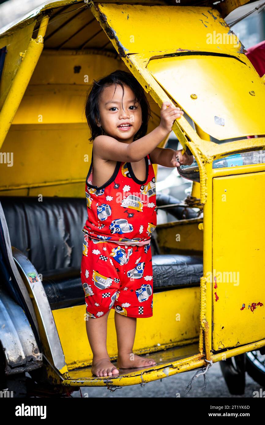 A cute Filipino girl plays on her fathers tricycle, pedicab or rickshaw in Ermita, Manila, Philippines. Stock Photo