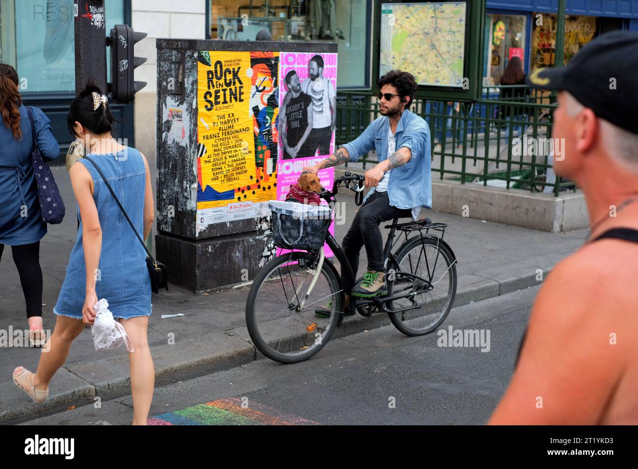 A Paris street scene a man on a bicycle stopped an a crossing near Hôtel de Ville with a dachshund in the handlebar basket, people, posters, street s. Stock Photo