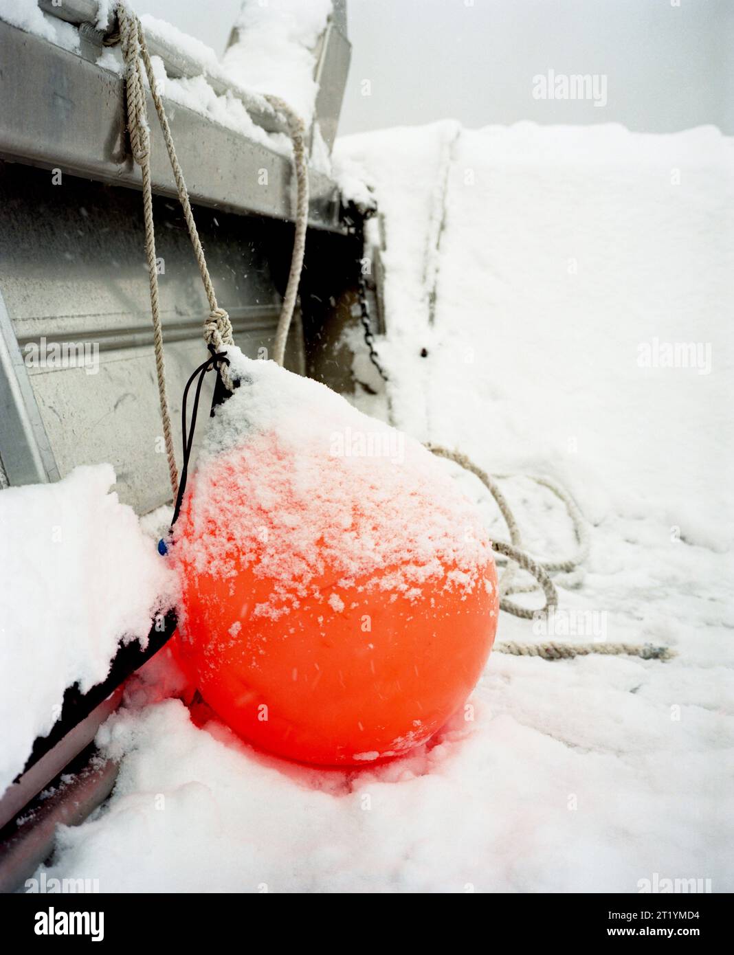 A big, orange buoy is covered in snow on the deck of a boat in the cold waters of Alaska. Stock Photo