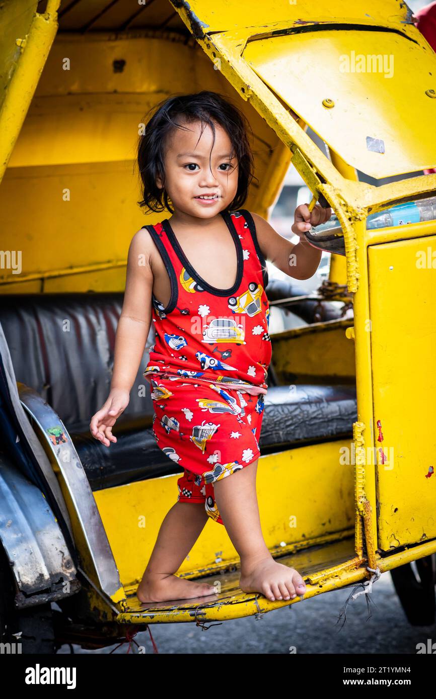 A cute Filipino girl plays on her fathers tricycle, pedicab or rickshaw in Ermita, Manila, Philippines. Stock Photo