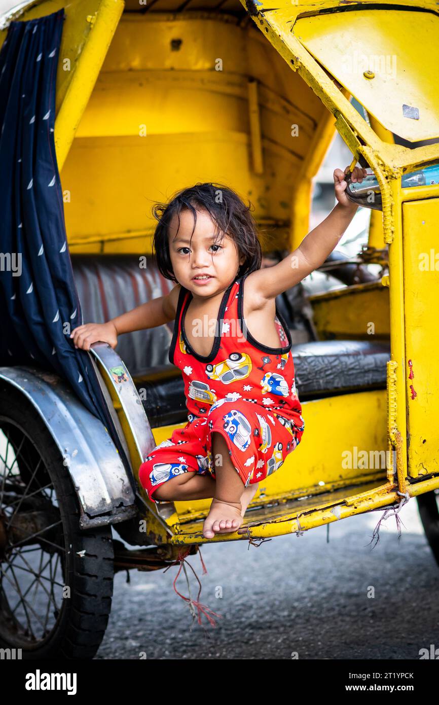 A cute Filipino girl plays on her fathers tricycle, pedicab or rickshaw