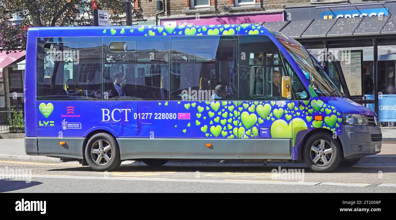 Heart graphics on blue single decker minibus run by Brentwood Community Transport independent charity a driver waits town centre stop Essex England UK Stock Photo