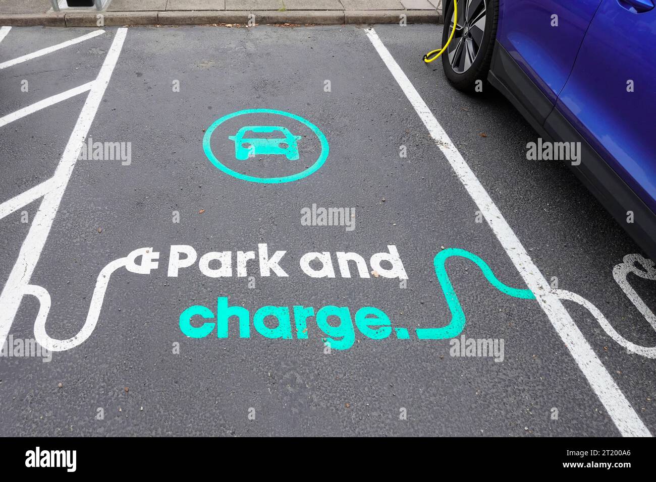 Close up view park and charge graphic painted on tarmac surface of car parking bay reserved for electric cars to top up at Holiday Inn Hotel Essex UK Stock Photo