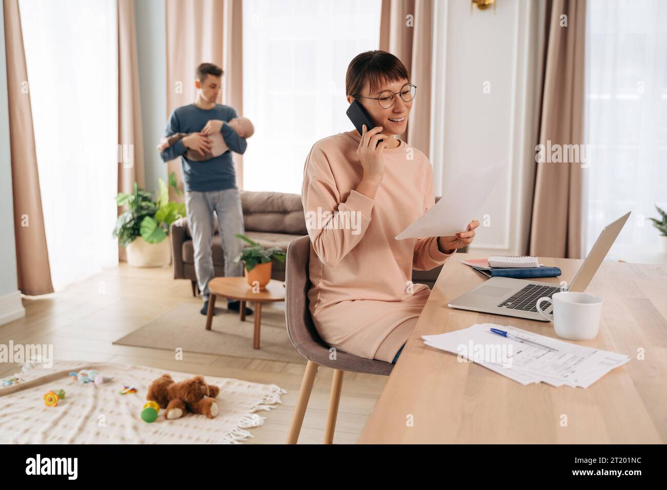 Happy working mother speaking over smartphone in her home office while ...