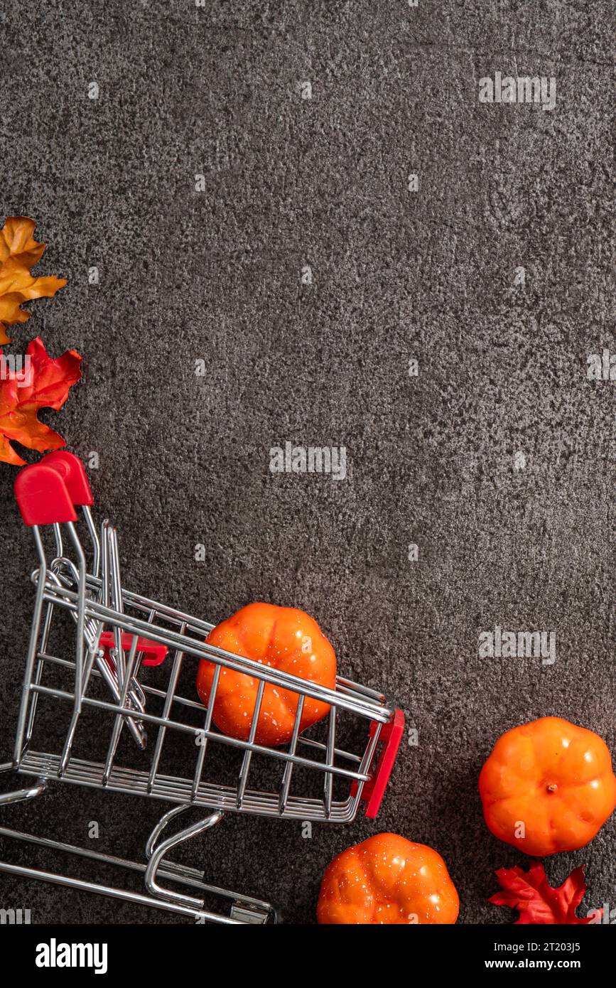 Autumn shopping design concept with shopping cart, maple leaves and pumpkin on black table background. Stock Photo