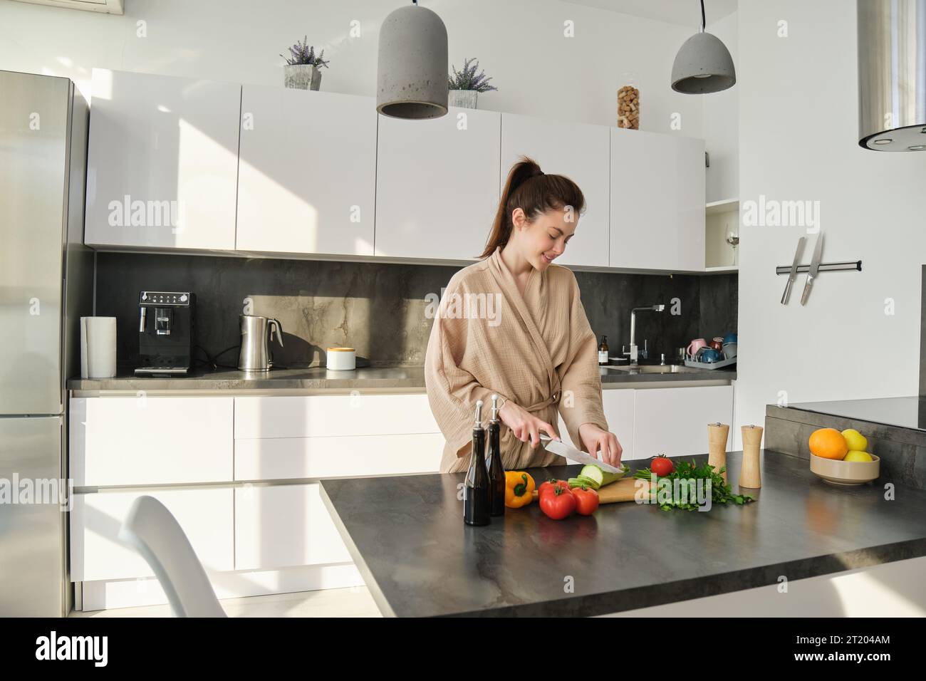Portrait of beautiful brunette girl chopping vegetables for meal, making salad in the kitchen, eating healthy food, preparing dinner. Stock Photo