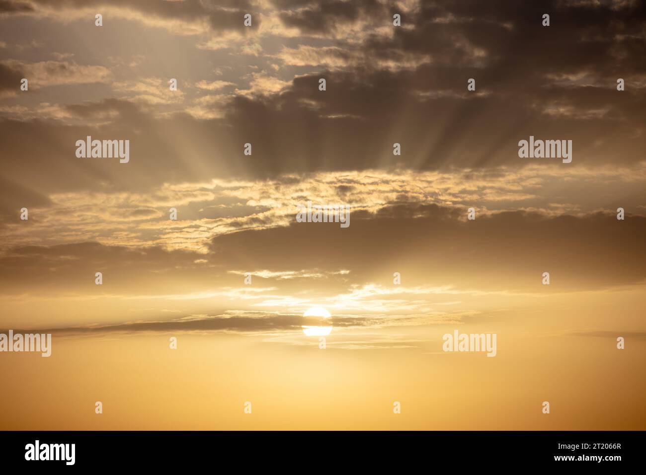 Sunset at cloudscape background. Sunbeam colors the sky, golden sun hides behind strange shaped cloud. Ad template for scary movie. Space Stock Photo
