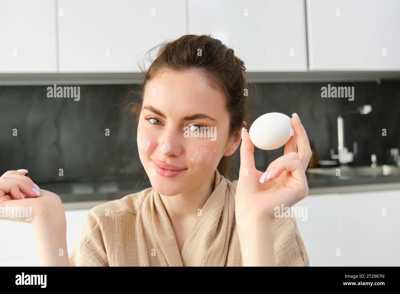 Attractive young cheerful girl baking at the kitchen, making dough, holding recipe book, having ideas. Stock Photo