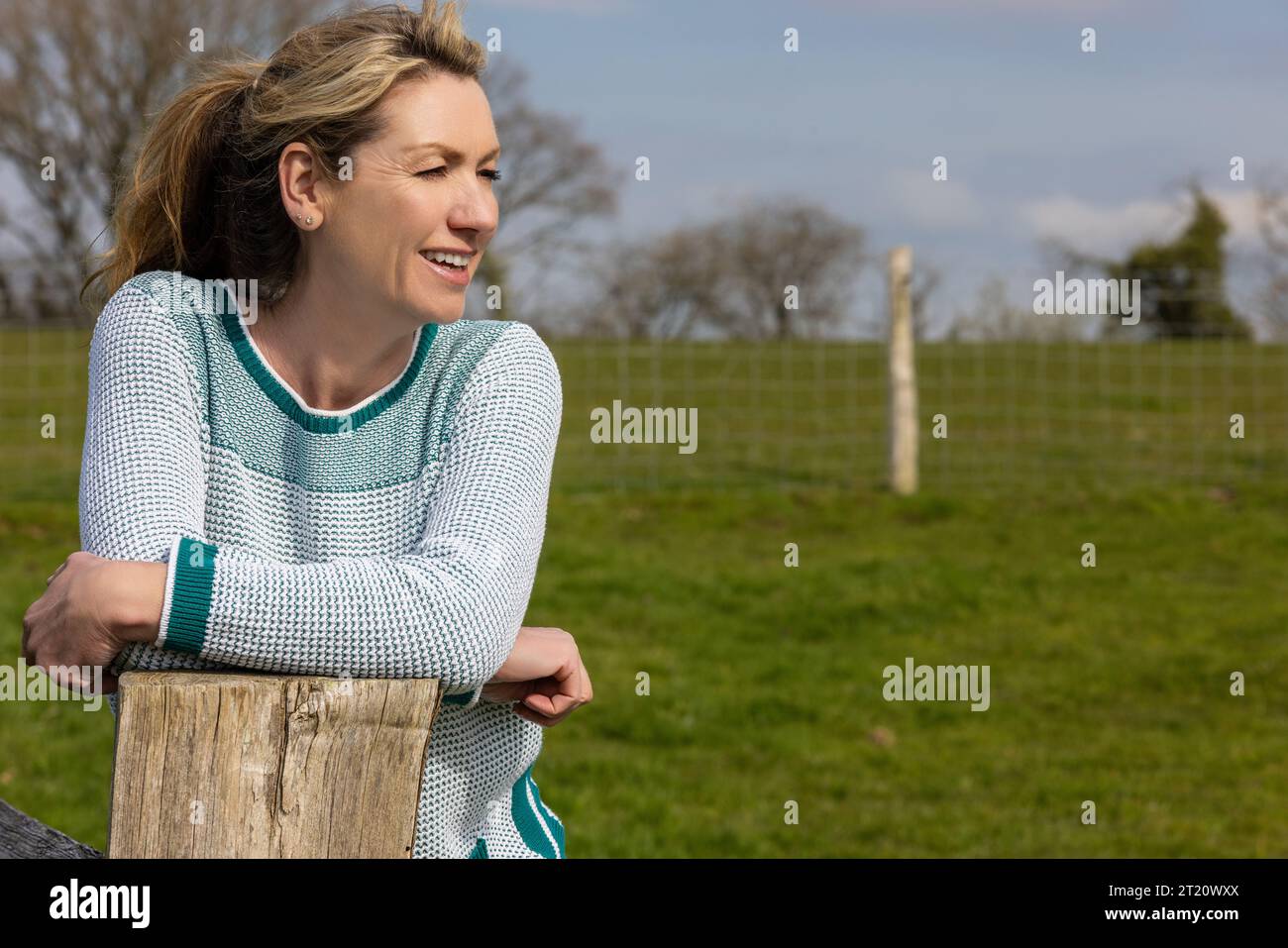 Attractive smiling happy middle aged woman leaning resting on fence in the countryside Stock Photo