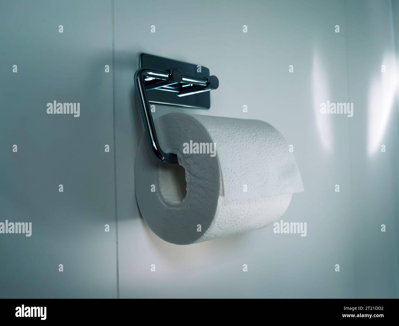Polished chrome toilet paper holder on a bathroom wall with green color grading to set a green ...