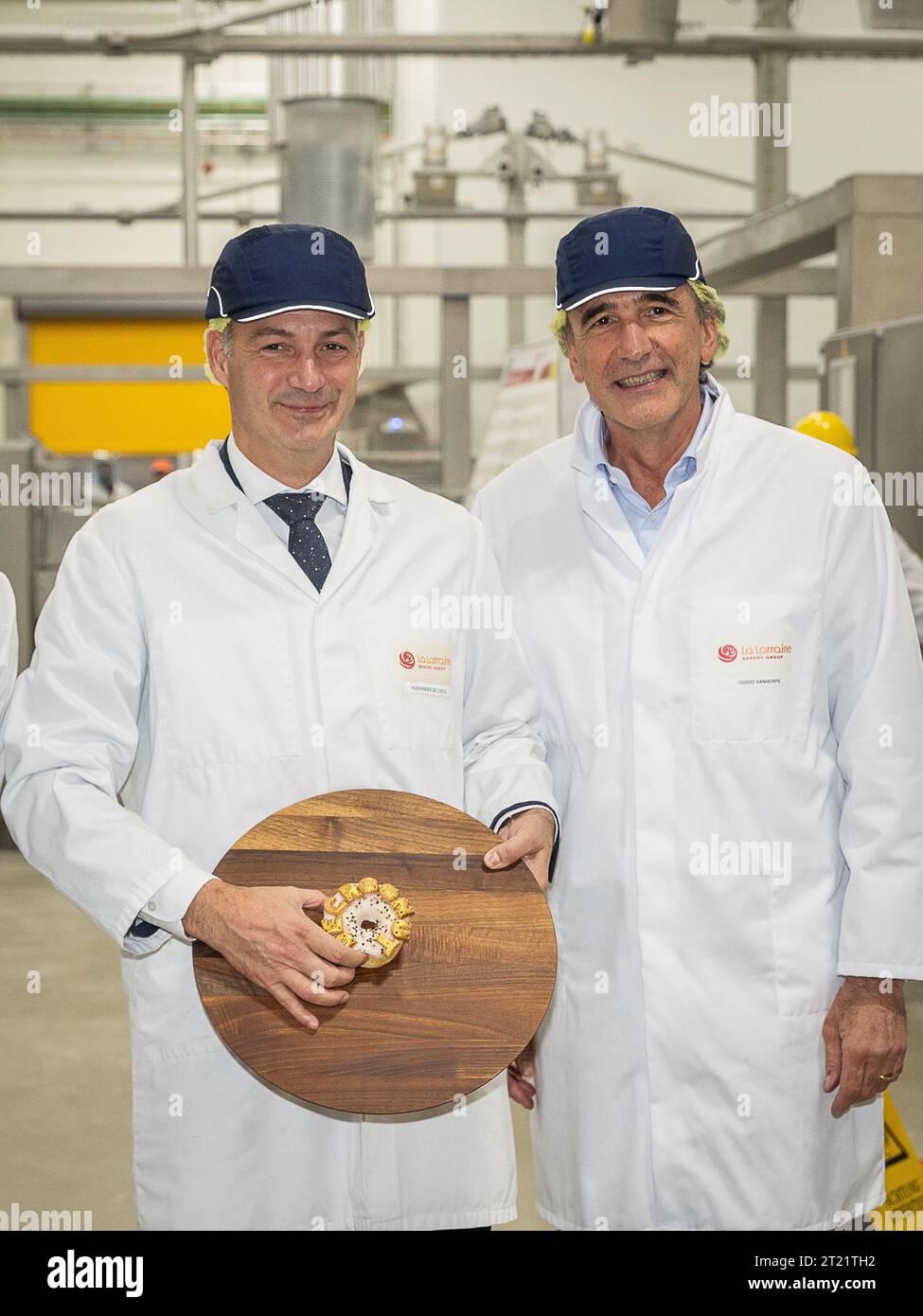 Erpe Mere, Belgium. 16th Oct, 2023. Prime Minister Alexander De Croo, holding a donut pastry with the word 'De Croonut' in gold-painted alphabet cookies (niknakjes) on top and La Lorraine Bakery Group CEO Guido Vanherpe pictured during a visit to the new production site of La Lorraine Bakery Group in Erpe-Mere, Monday 16 October 2023. BELGA PHOTO JAMES ARTHUR GEKIERE Credit: Belga News Agency/Alamy Live News Stock Photo