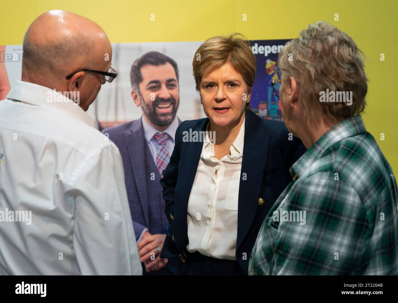 Aberdeen, Scotland, UK. 16th October 2023.  Day two of the SNP annual conference and former First Minister Nicola Sturgeon makes an appearance. A media frenzy followed before she made her way into the conference venue to listen to the afternoon’s proceedings. Nicola Sturgeon at the independence stall overlooked by a poster of First Minister Humza Yousaf.  Iain Masterton/Alamy Live News Stock Photo