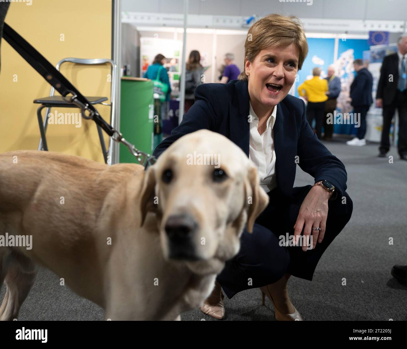 Aberdeen, Scotland, UK. 16th October 2023.  Day two of the SNP annual conference and former First Minister Nicola Sturgeon makes an appearance. A media frenzy followed before she made her way into the conference venue to listen to the afternoon’s proceedings. Nicola Sturgeon overcomes her fear of dogs to pet Sammy the guide dog. Iain Masterton/Alamy Live News Stock Photo
