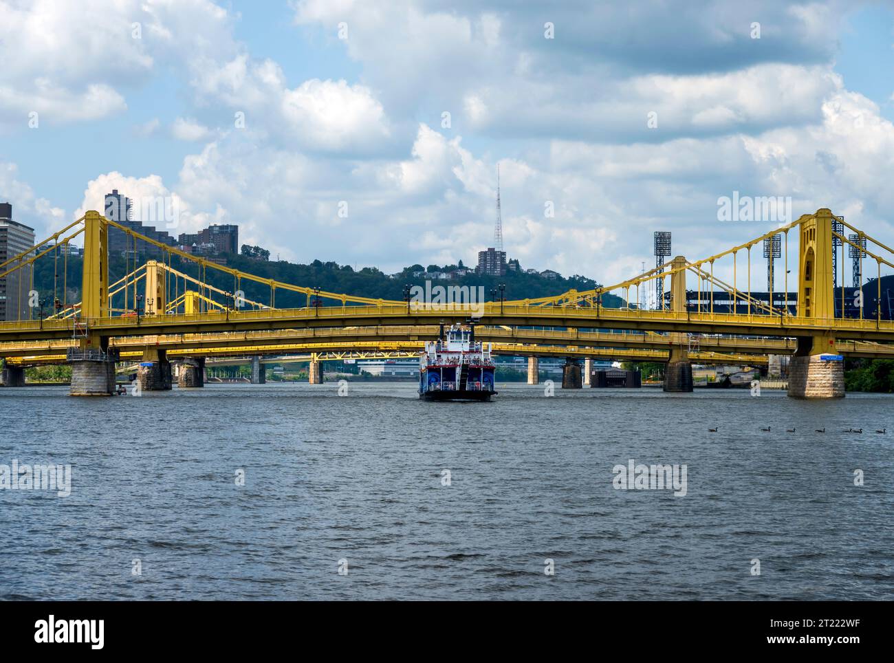 A tourist boat passes under the three yellow suspension bridges on the Allegheny River, Pittsburgh, Pennsylvania. Stock Photo
