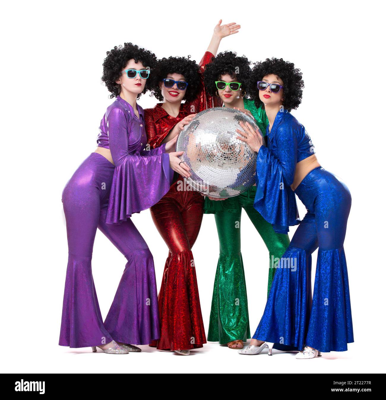 A group of girls in disco costumes are holding a disco ball and looking at the camera. Stock Photo