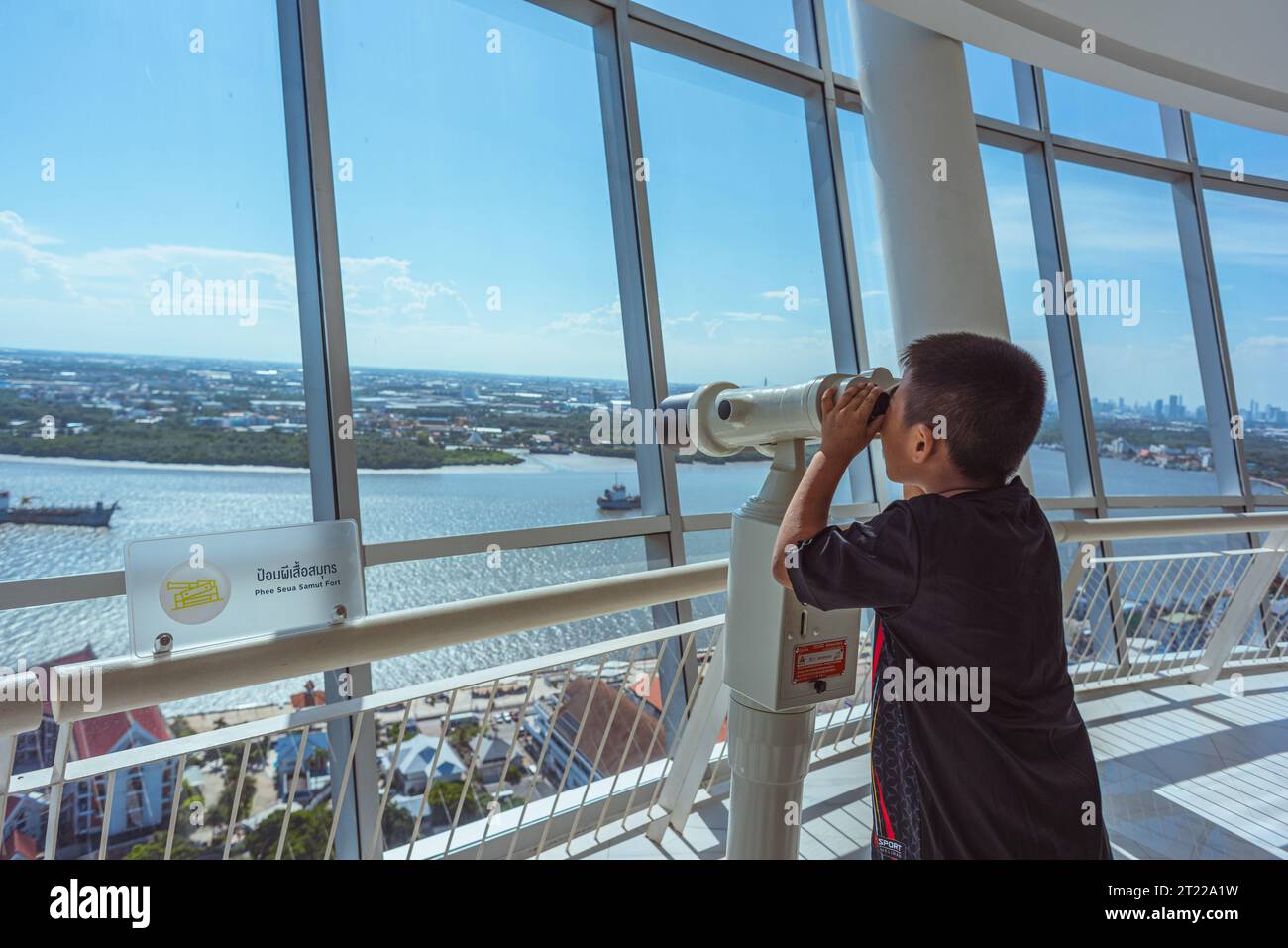 Samut Prakan, Thailand - September 3, 2023: a boy looks at the Chao Phraya River's shores through binoculars at observation deck of Samut Prakan Tower Stock Photo
