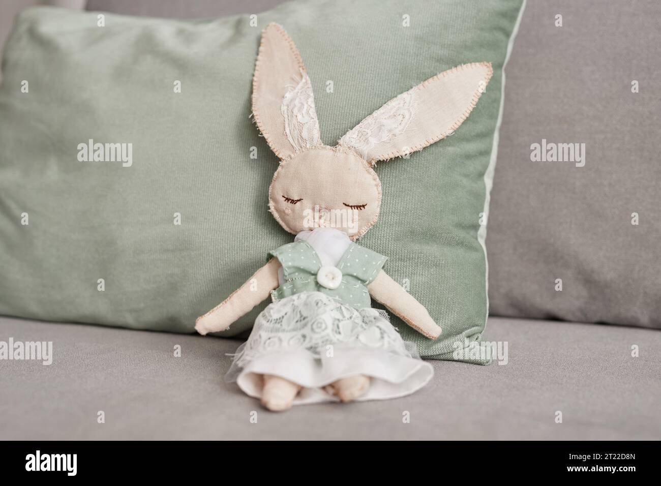 Close up of handmade bunny toy sitting on sofa and wearing cute lace dress, copy space Stock Photo