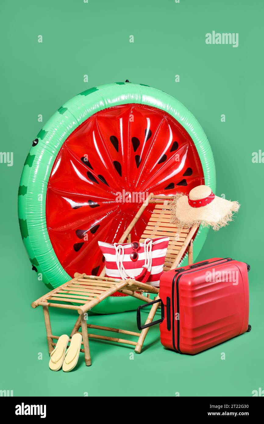 Deck chair, suitcase and beach accessories on green background Stock Photo
