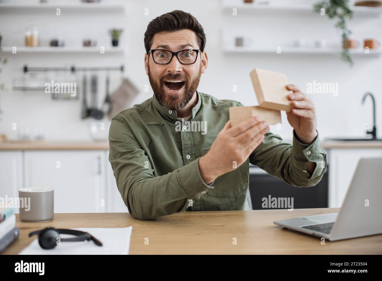 View from smartphone camera of emotional man in casual clothes experiencing pleasant shock while looking inside parcel box. Technology blogger satisfi Stock Photo
