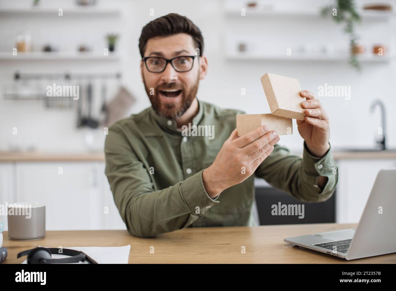 View from smartphone camera of emotional man in casual clothes experiencing pleasant shock while looking inside parcel box. Technology blogger satisfi Stock Photo