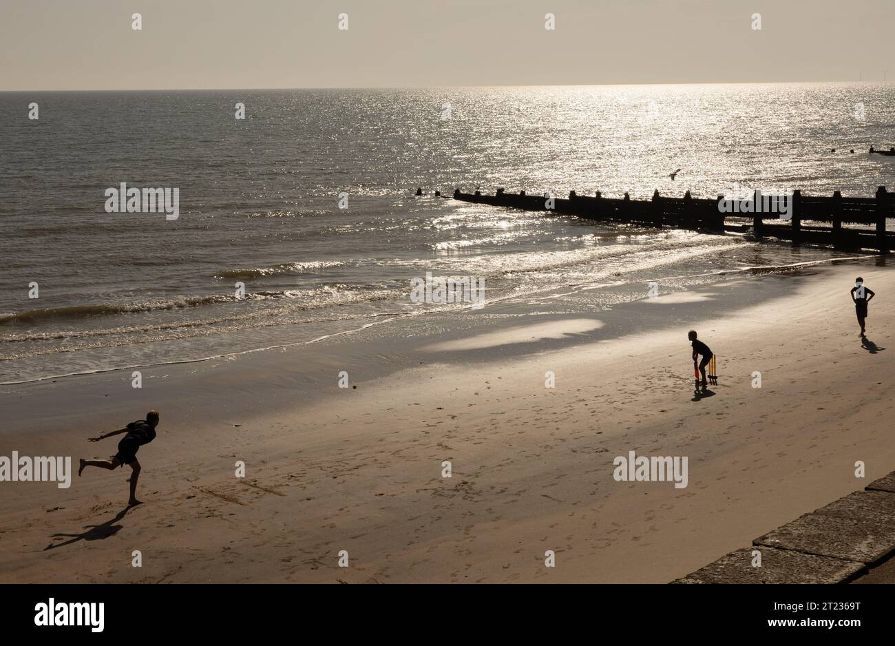 Silhouetted figures playing cricket on the beach at seaside Stock Photo