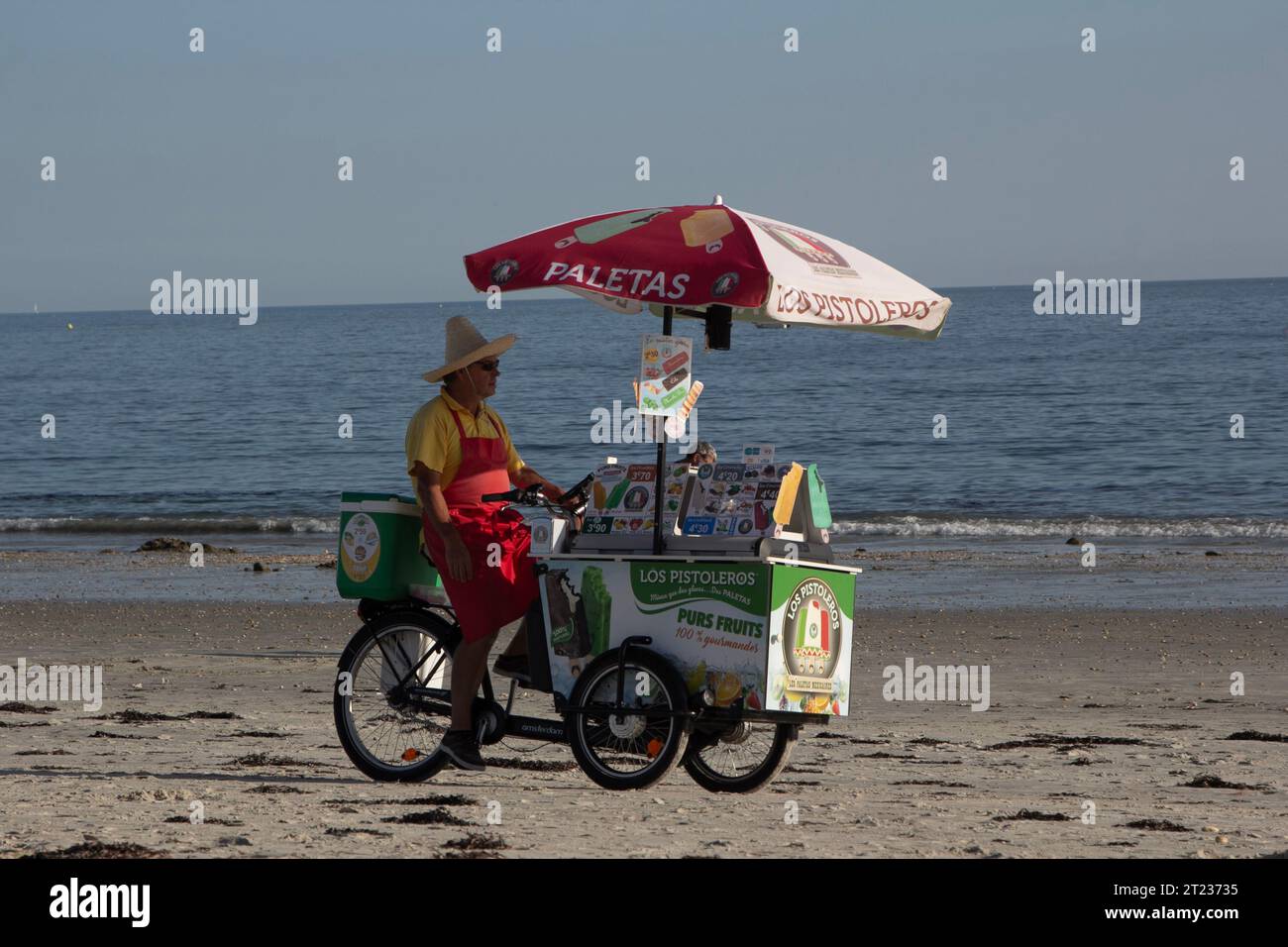 A man peddles his ice-cream cart on the beach in Carnac, Brittany, France, on an afternoon in late summer. Stock Photo