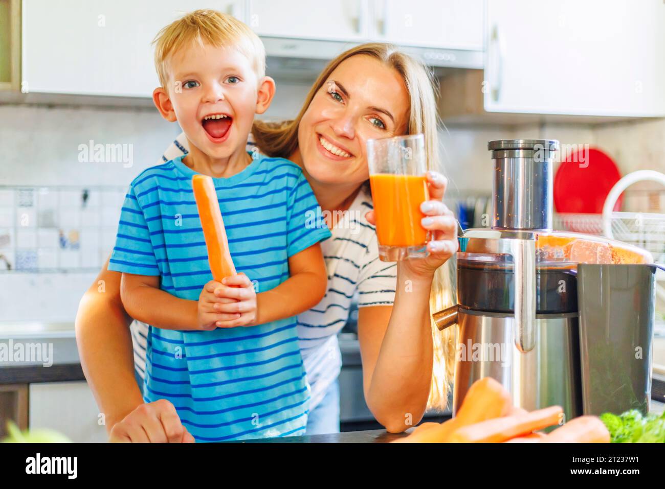 Mom and son drink fresh carrot juice squeezed using juicer in kitchen at home Stock Photo