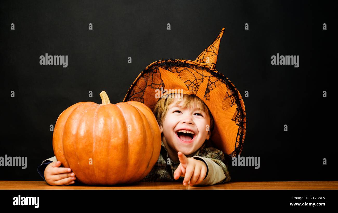 Preparation Halloween holiday. Happy child in witch hat with Halloween pumpkin pointing finger at you. Little kid wizard with Jack-o-lantern. Trick or Stock Photo