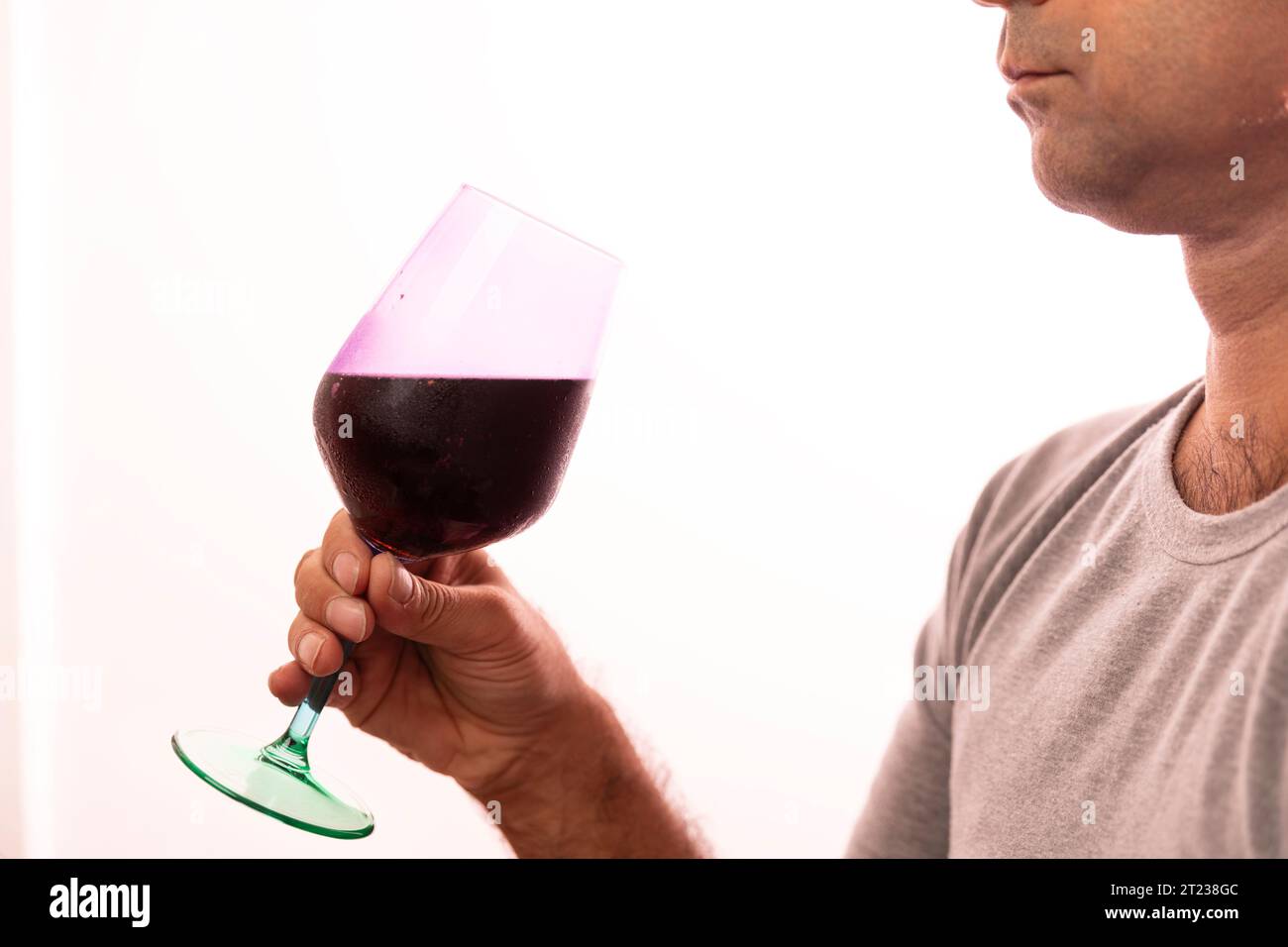 Unrecognizable caucasian man in 40s wearing a gray t shirt holding a wineglass full of red wine. Stock Photo