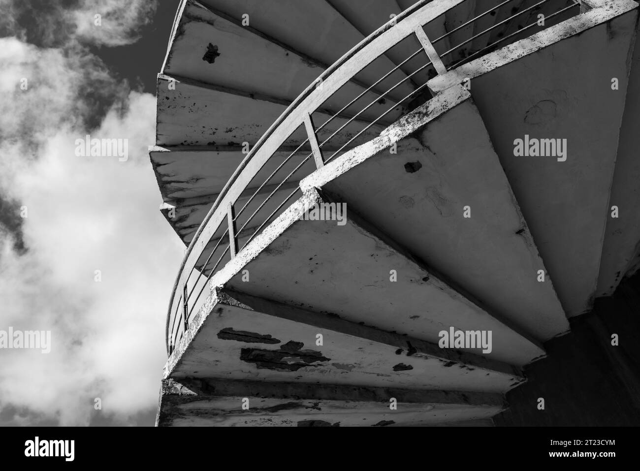Grungy spiral ladder is under cloudy sky, abstract architectural photo. Black and white photo Stock Photo