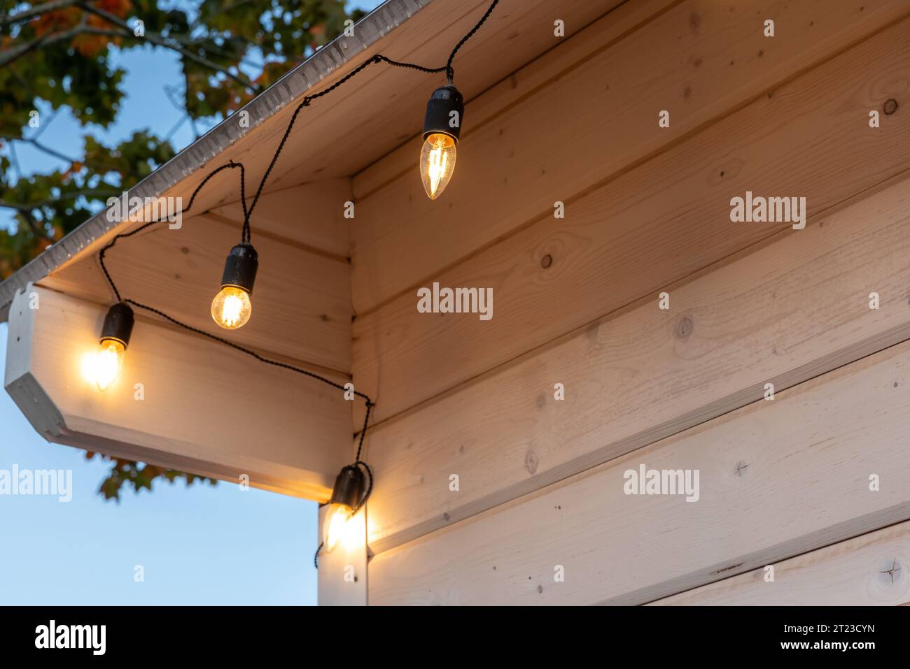 Garland of light bulbs hanging on a wooden house, close up Stock Photo