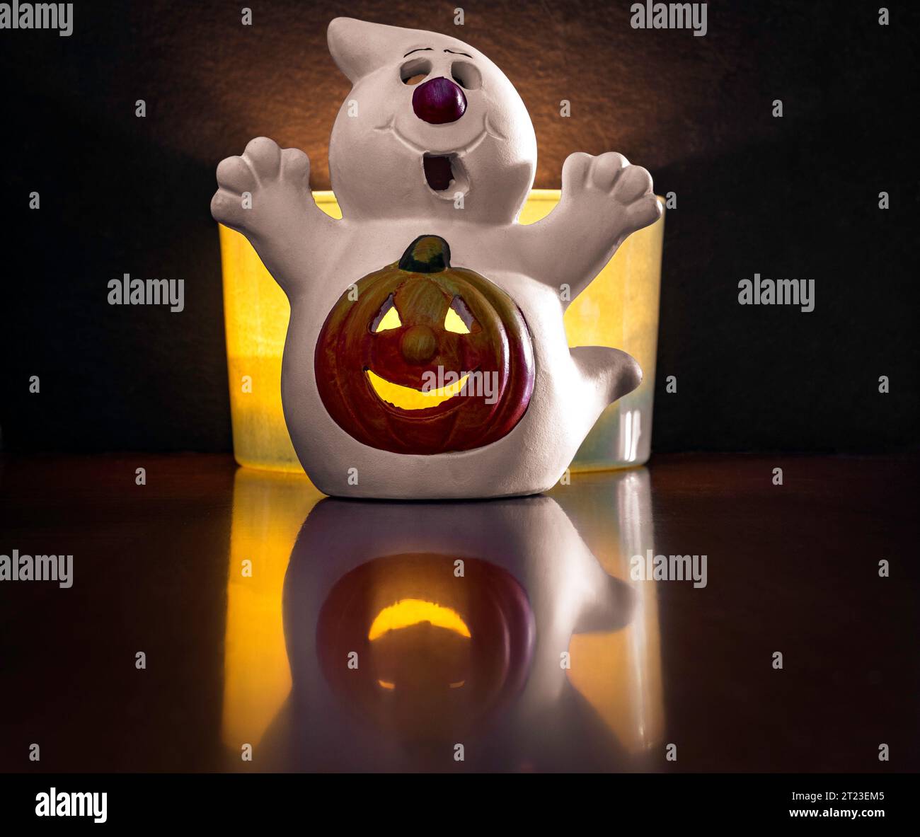 A plaster ghost with a funny Halloween pumpkins in the middle. Decoration placed on a wooden surface with a black background and light reflections. Stock Photo
