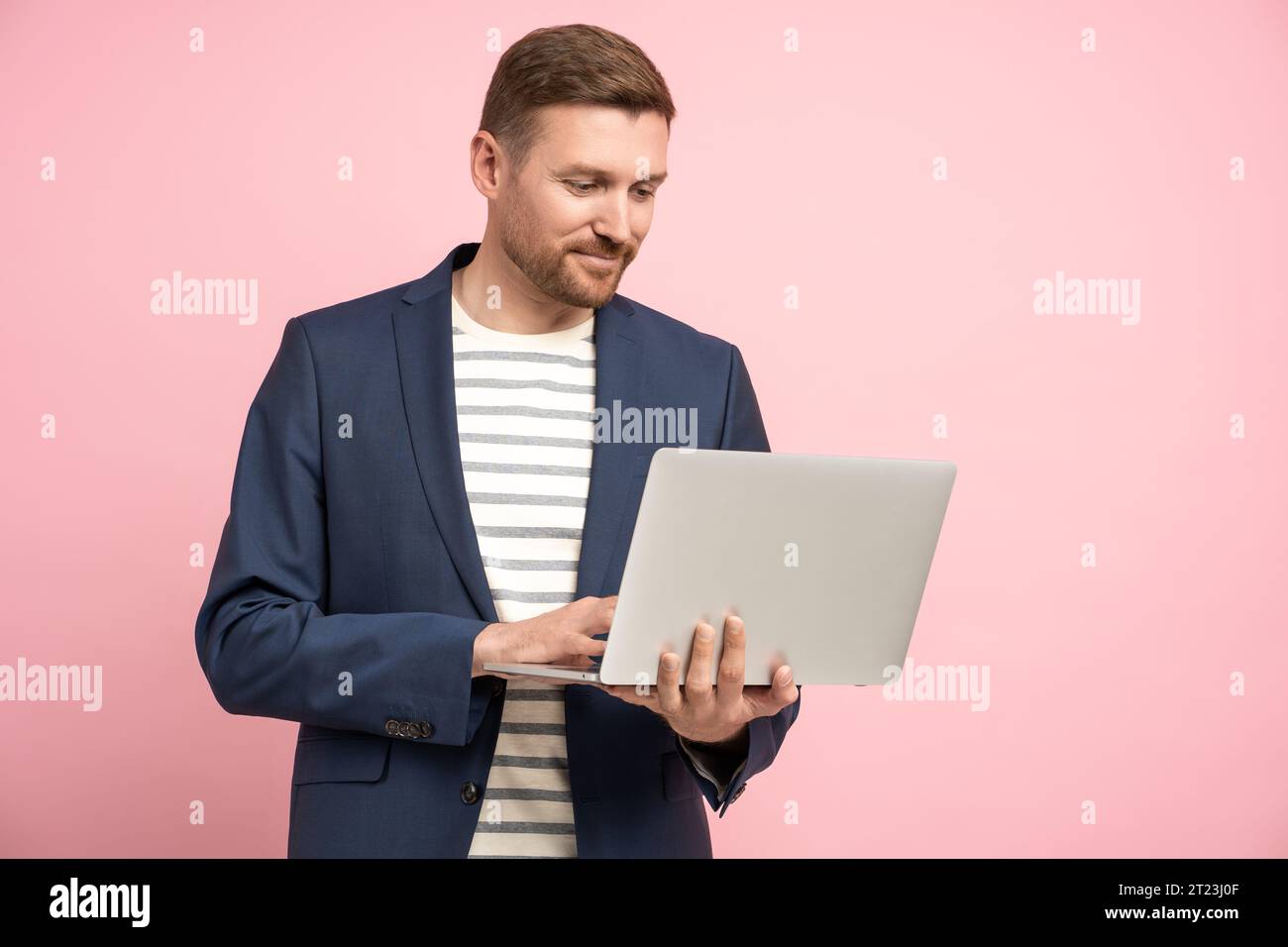 Pensive businessman with laptop isolated on pink wall working, types, chatting about work, business Stock Photo