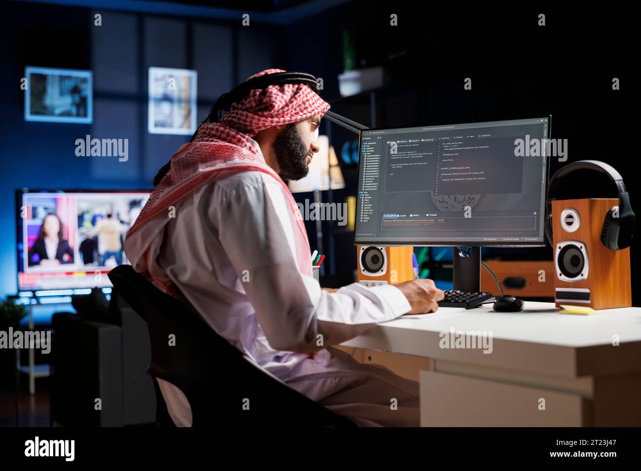 Dedicated software programmer wearing traditional Arabic clothing is seated at his home office desk examining database code on computer. Muslim man checking the programming language on the pc monitor. Stock Photo