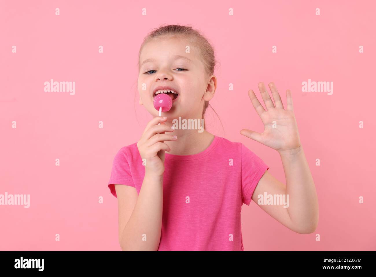 Cute little girl licking lollipop on pink background Stock Photo