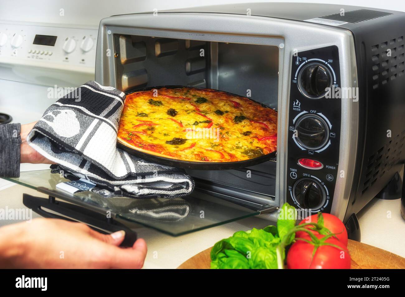 Hands removing a cooked pizza from a small bench top oven Stock Photo