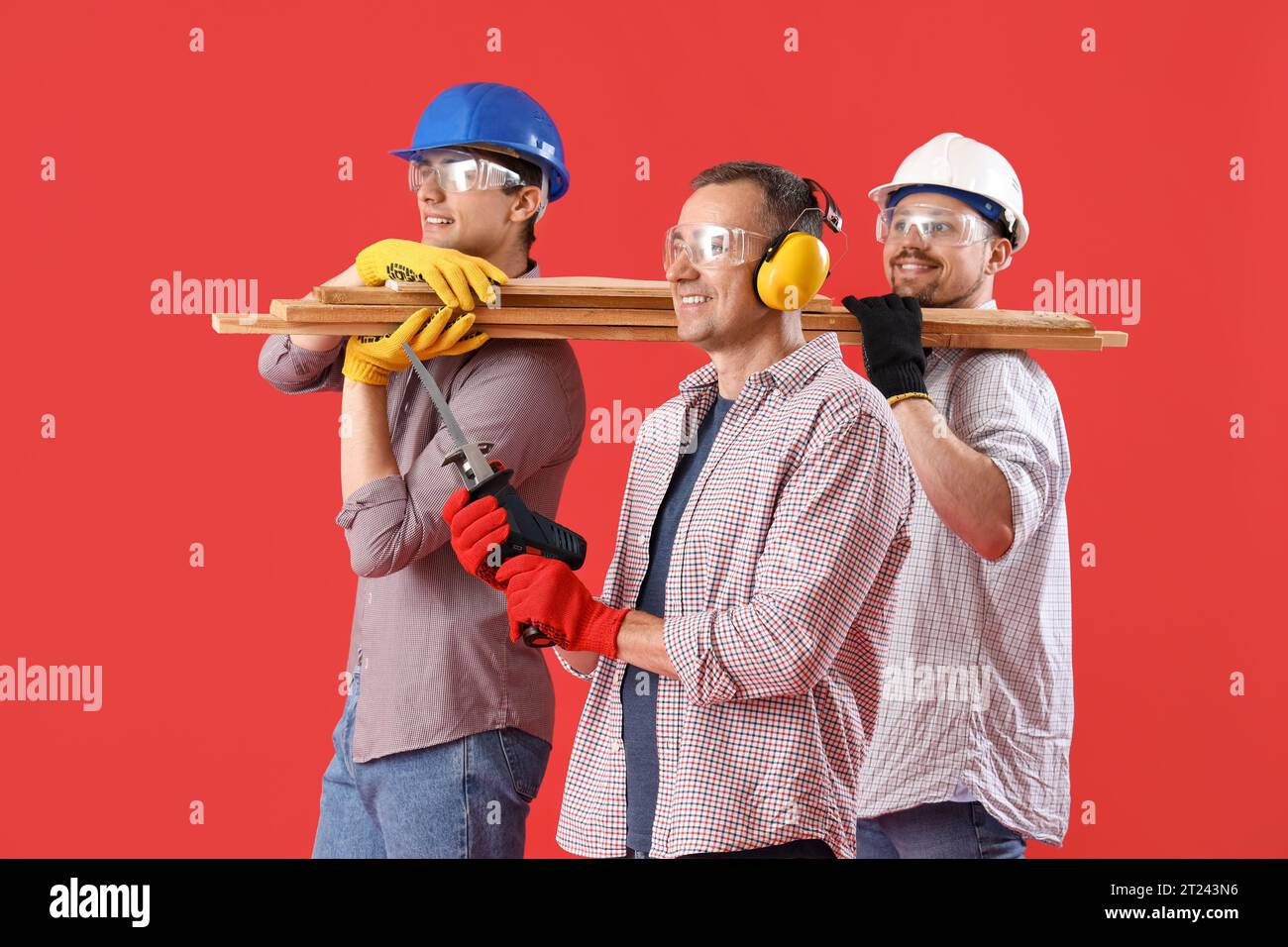 Team of male builders with wooden planks on red background Stock Photo